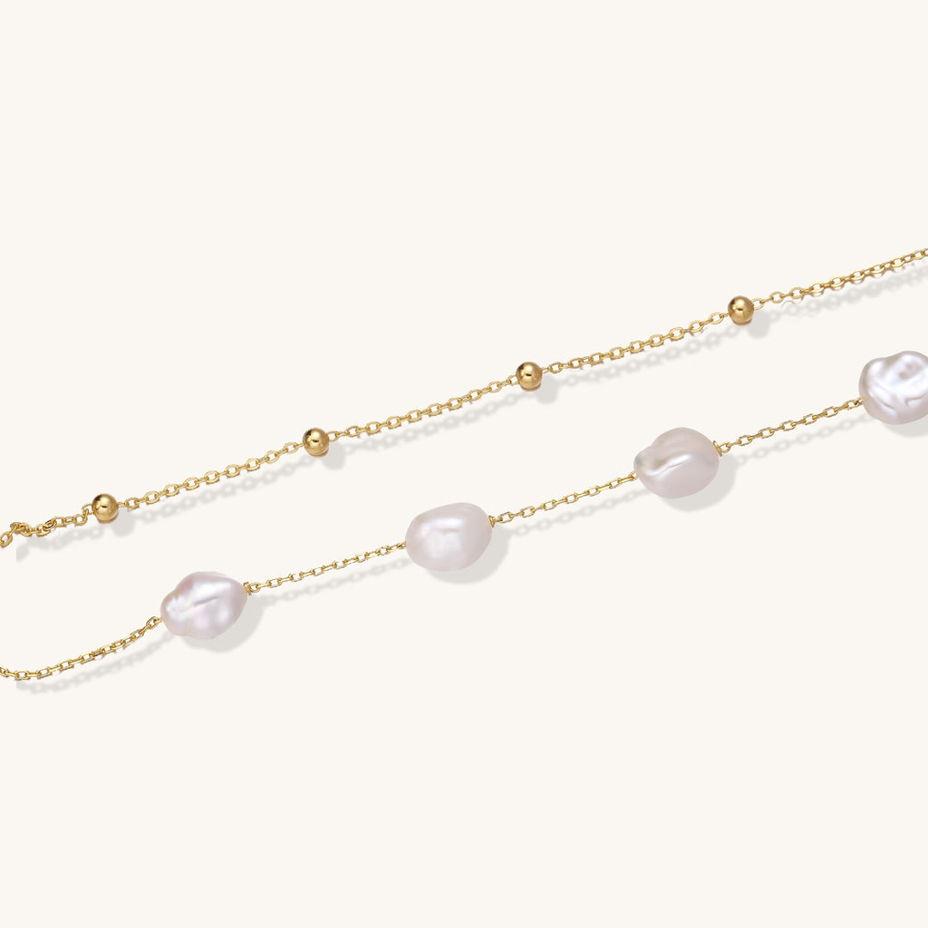 Delicate multi-layered gold-plated bracelet with irregular baroque pearls and freshwater pearls on cream background.