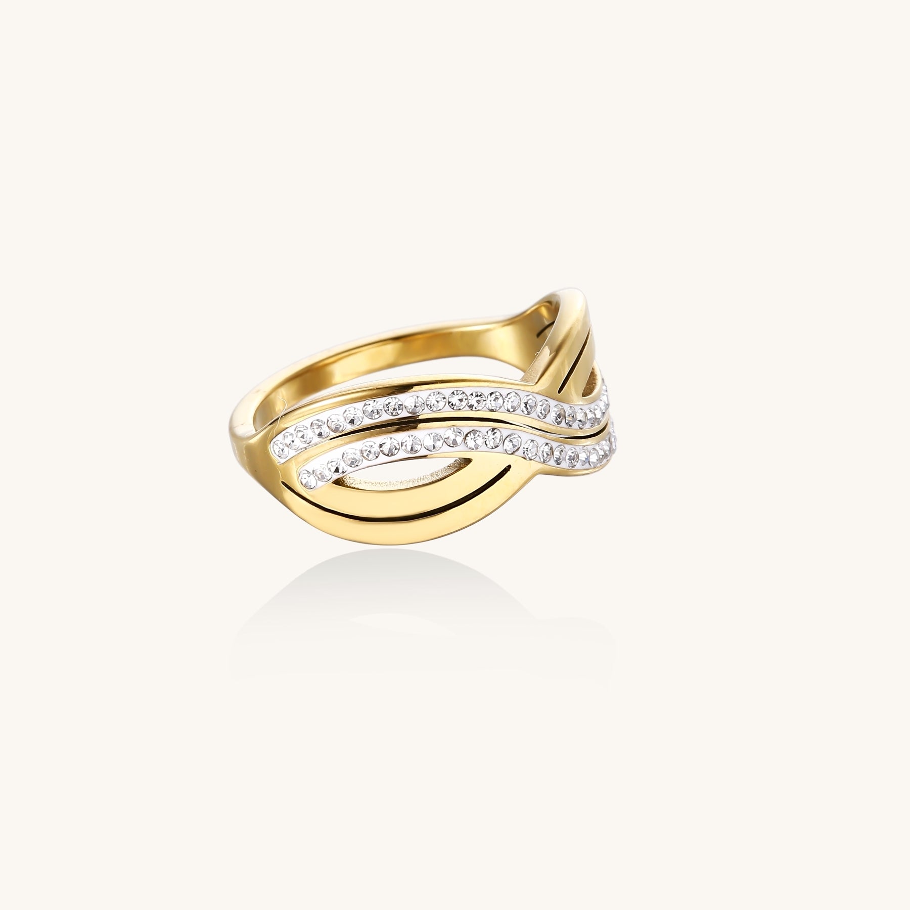 Gold-plated stainless steel ring with crossed infinity bands adorned with sparkling rhinestones against cream background.