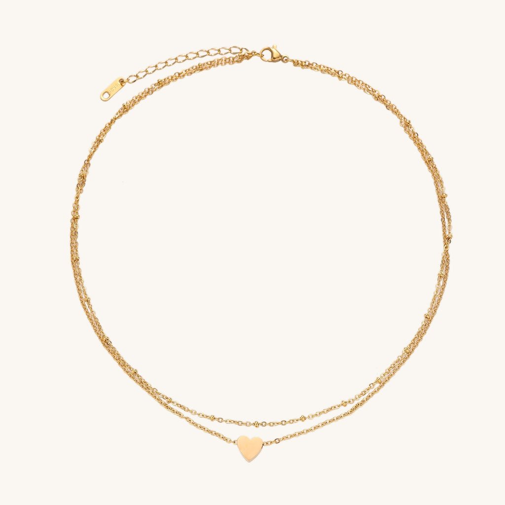 Two-layer gold-plated stainless steel necklace with small heart pendant displayed on beige background