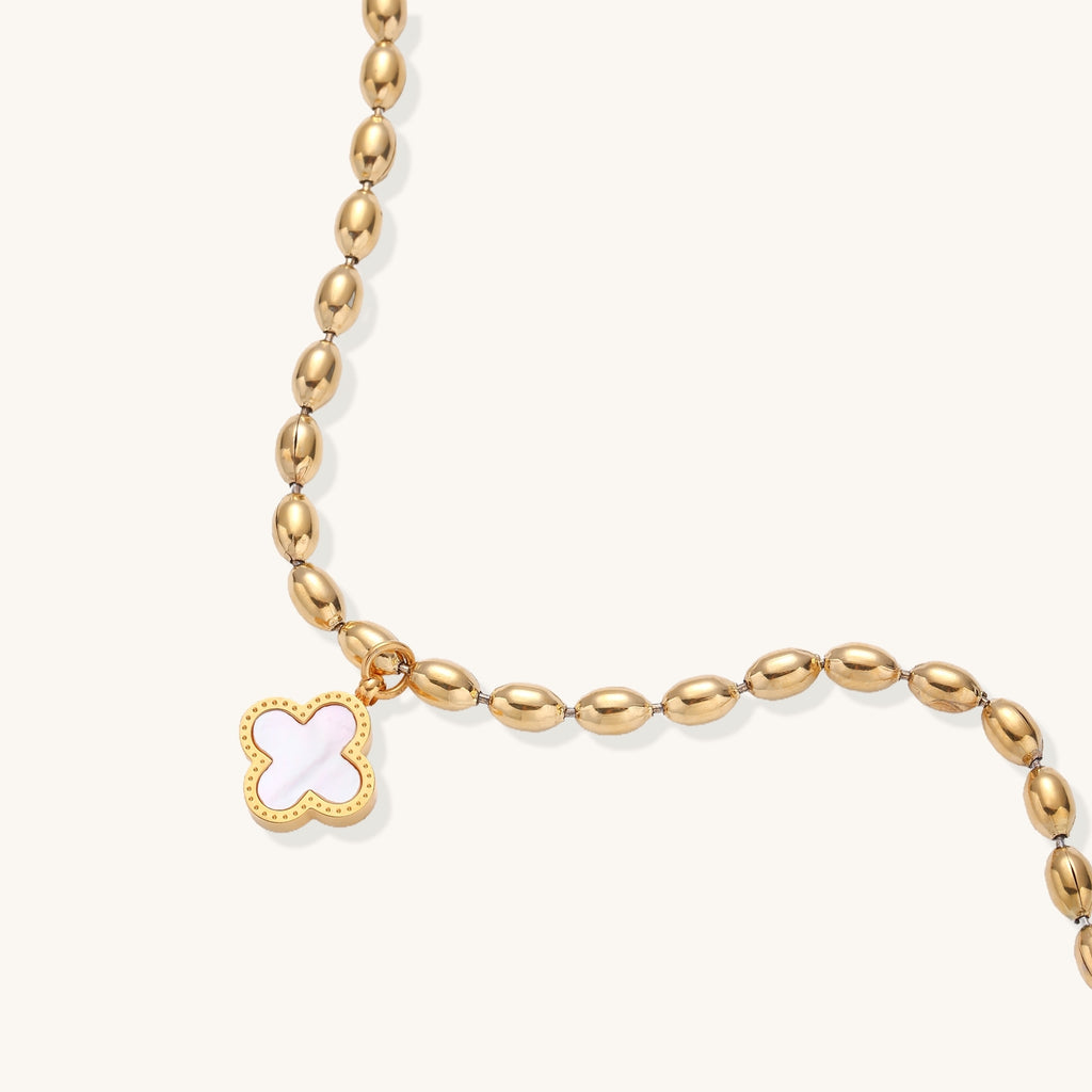 Dainty gold-plated beaded bracelet with oval links and four-leaf clover charm pendant on neutral background.