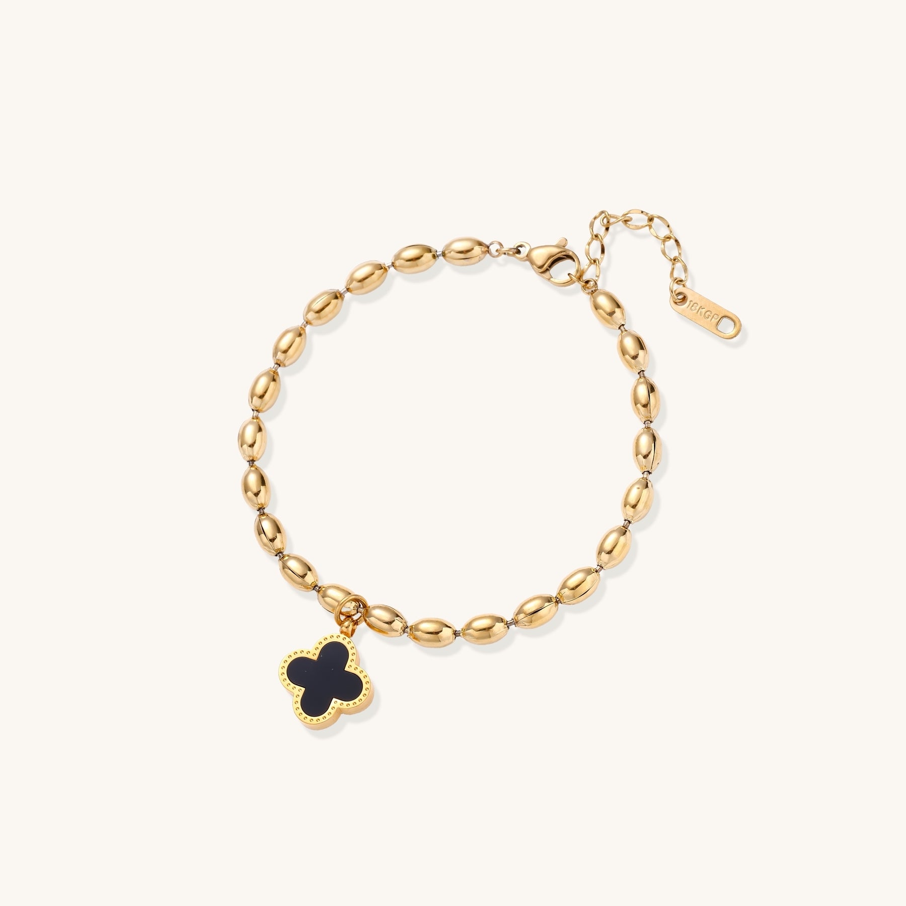 Dainty gold-plated beaded bracelet with oval links and four-leaf clover charm pendant on neutral background.