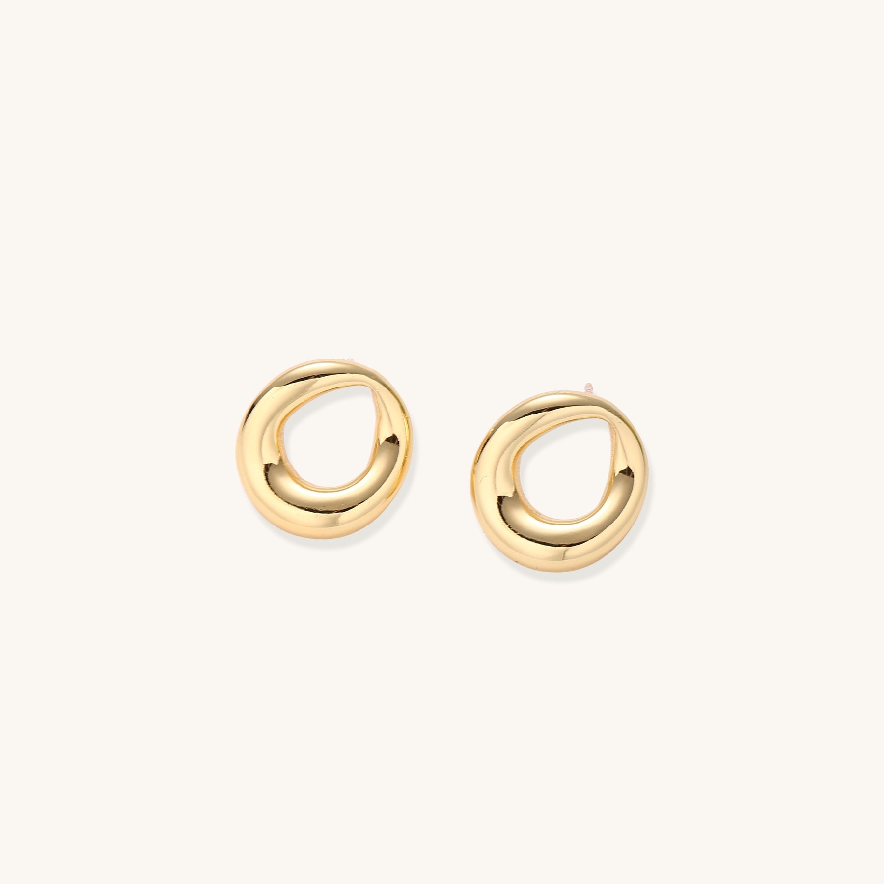 Pair of polished 18K gold-plated stainless steel oval loop stud earrings on cream background