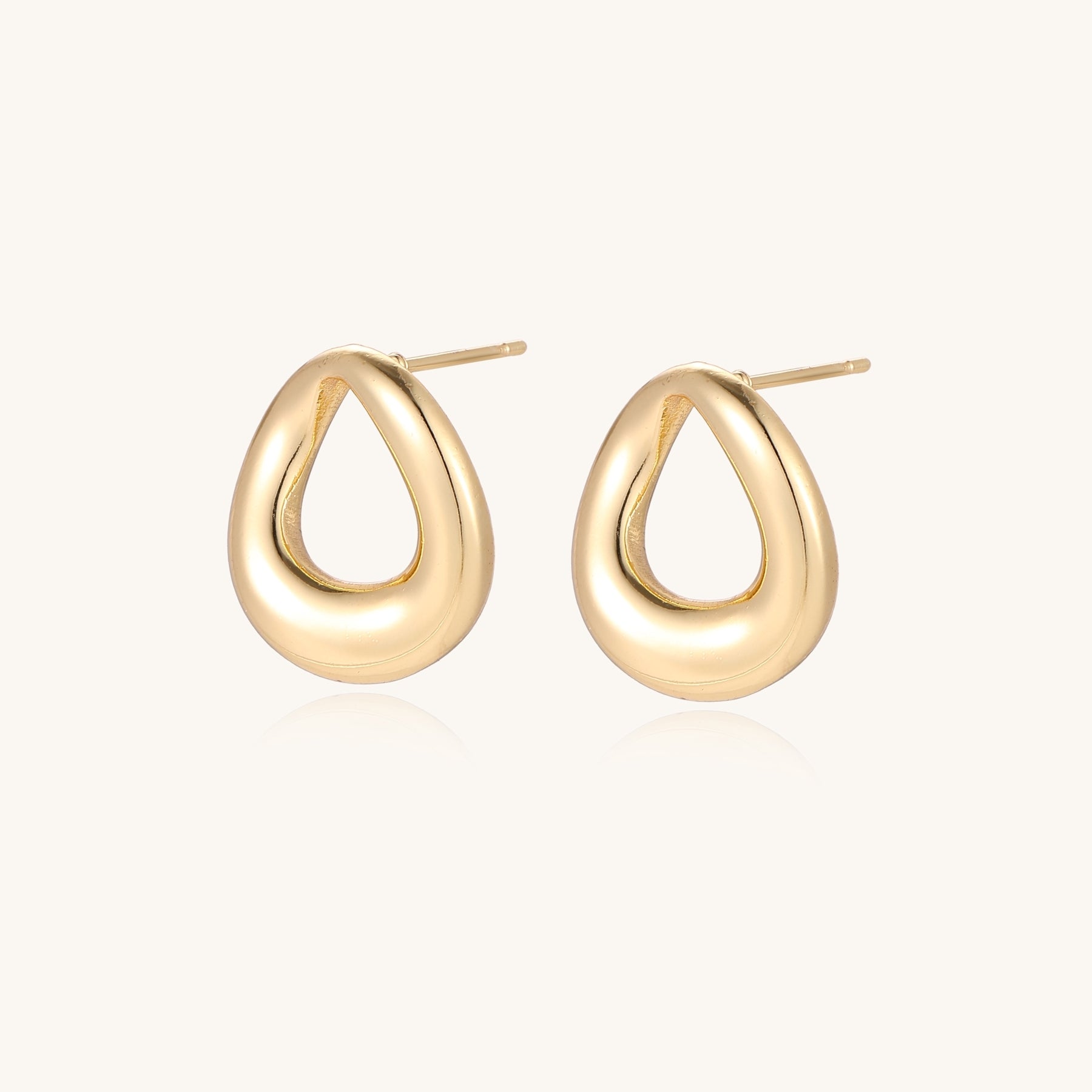 Pair of polished 18K gold-plated stainless steel oval loop stud earrings on cream background