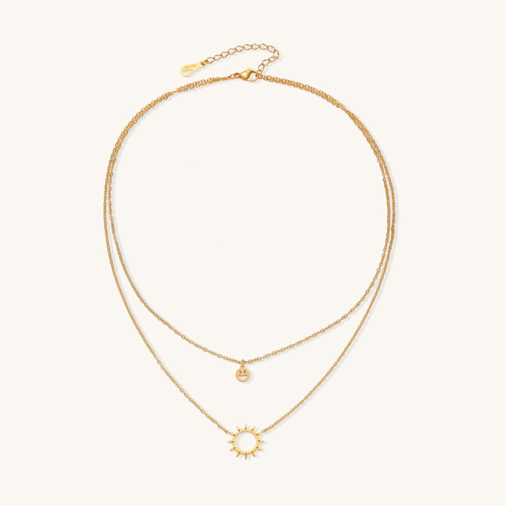 Delicate gold-plated layered necklace with smiley face and sun pendants on white background, showing adjustable chain.